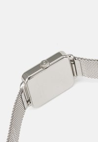Zilveren gaasband horloge met een rechthoekige kast, gepolijste metalen afwerking en kroon aan de zijkant. Bevat een minimalistisch ontwerp en gegraveerde details.