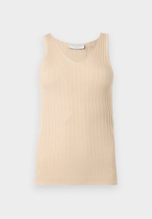 Žena nosiaca béžový bezrukávový rebrovaný top, krémovú midi sukňu s predným rozparkom a bordové baleríny Mary Jane, stojaca pred jednoduchým pozadím.