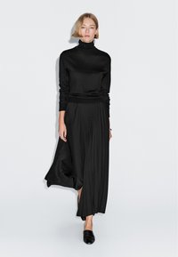 Zwarte coltrui gecombineerd met een geplooide zwarte maxi rok. Soepele textuur, getailleerde top, vloeiend ontwerp en een zijsplit detail.