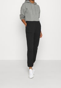 Sweat à capuche gris coupé avec cordons, associé à un pantalon noir fuselé avec des poches latérales, porté avec des baskets blanches.
