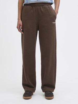 Brune, løstsittende joggebukser med elastisk midje og sidelommer, med en liten hvit logo på venstre lår.