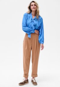 Jasnoniebieska bluzka z wiązanym dekoltem, beżowe spodnie o wysokim stanie oraz trampki w leopardzi wzór. Gładki materiał i luźny krój.