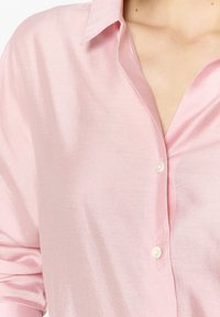 Lichtroze, zijden blouse met een kraag en parelknopen. Heeft een gladde textuur en een losse pasvorm met opgerolde mouwen.