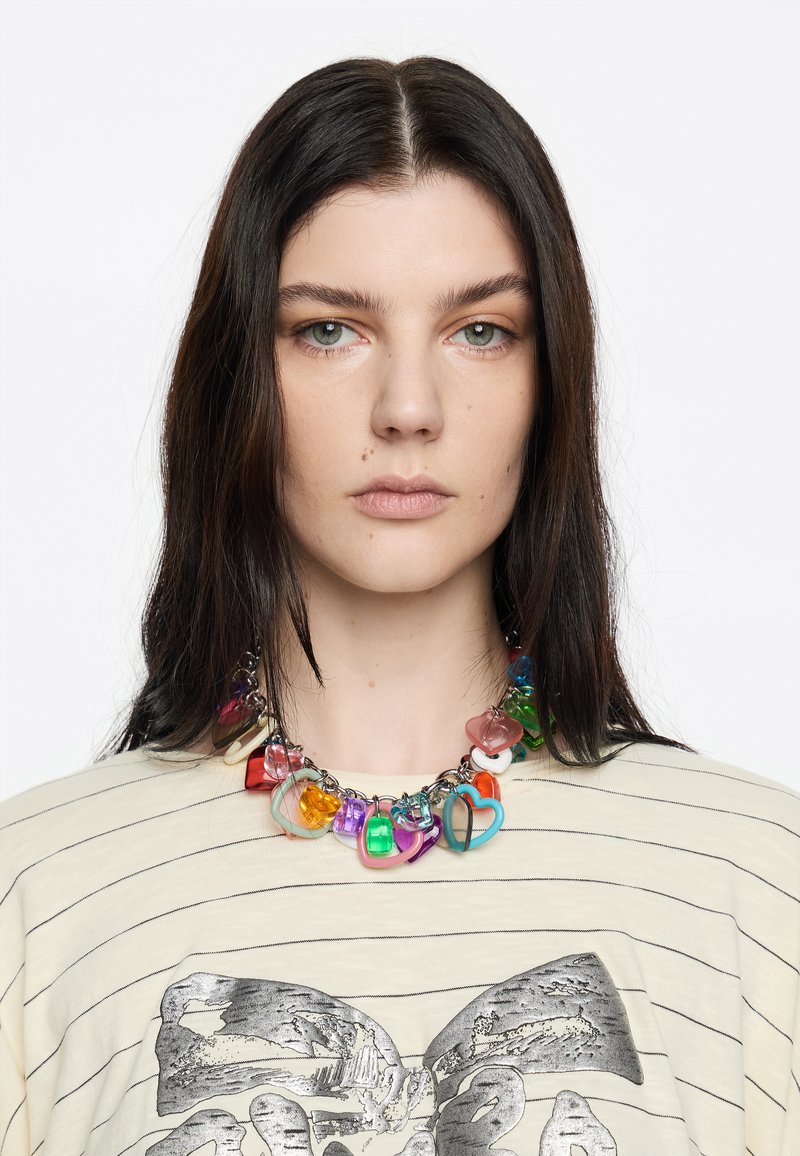 Kleurrijke chunky ketting van verschillende vormen van doorzichtige plastic kralen in rood, blauw, groen en paars, op een zilveren ketting.