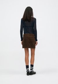 Jupe en velours côtelé marron au design ajusté, associée à un haut à manches longues côtelé bleu marine et des chaussettes rayées. Chaussures : mocassins noirs.