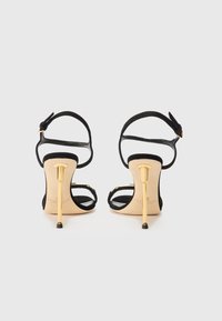 Black suede high-heeled sandals with a gold stiletto heel and ankle strap. Features minimalistic design and open-toe construction.