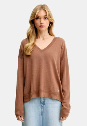 Maglione marrone a V con maniche lunghe, polsini e orlo a coste, tessuto textured, abbinato a jeans azzurri chiari. Presenta un accento logo sull'orlo.