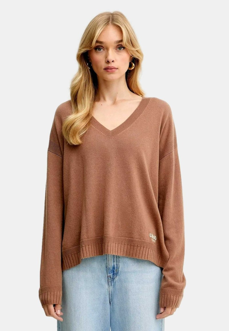 Maglione marrone a V con maniche lunghe, polsini e orlo a coste, tessuto textured, abbinato a jeans azzurri chiari. Presenta un accento logo sull'orlo.
