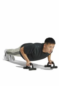 Push-up bars van zwart rubber met grip handgrepen. Een persoon in een donker shirt en lichte broek demonstreert een push-up positie op de bars.
