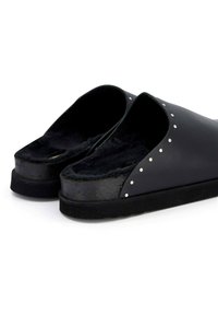 Black slip-on shoes with a soft fur lining, curved design, flat sole, and silver stud accents along the upper edge.