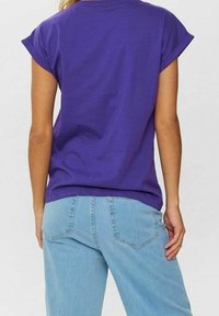 Violetti puuvillainen t-paita käännettyine hihoineen, yhdistetty vaaleansinisiin farkkuihin. T-paidassa on rento istuvuus ja yksinkertainen muotoilu.