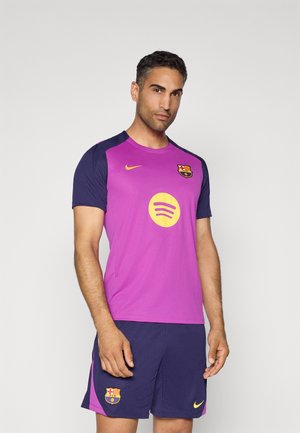 FC Barcelona Nike trøje i pink med blå ærmer, har rund halsudskæring, klublogo og Spotify-logo i gul. Parret med navy shorts.
