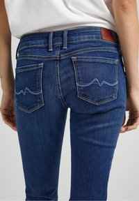 Mörkblå denimjeans med en åtsittande design, smala ben och dekorativt broderi på bakfickorna. Har en läderetikett på midjebandet.