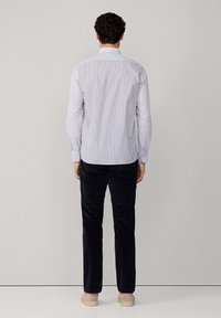 Camicia a righe blu chiaro e bianca con maniche lunghe, polsini con bottoni, indossata con pantaloni scuri. Design semplice e taglio classico.