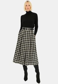 Czarny sweter z golfem w połączeniu z czarno-białą spódnicą w kształcie litery A w kratę, podkreśloną szerokim czarnym paskiem. Całość dopełniają zamszowe kozaki do kolan.