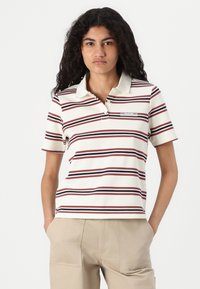 Randig polo t-shirt i kräm, röd och marin färg, med korta ärmar och spetsig krage. Innehåller en varumärkesetikett på bröstet.