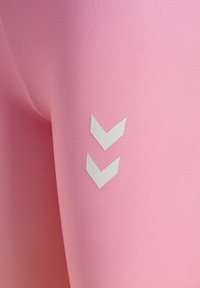Roze sportlegging van gladde, rekbare stof met twee witte chevronlogo's aan de buitenkant van het been.