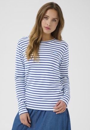 Chemise à manches longues rayée en coton blanc et bleu, avec un col rond et un petit emblème en forme de cœur bleu sur la poitrine.
