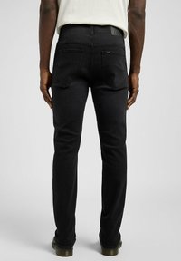 Czarne dżinsy z denimu o wąskim kroju, z talią średniej wysokości, tylnymi kieszeniami z zakrzywionymi szwami oraz skórzaną naszywką marki na talii.