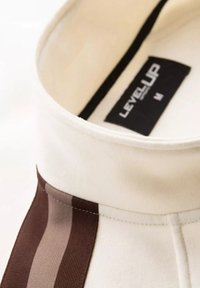 Chemise col classique en tissu crème avec des rayures brunes et beiges. L'étiquette indique "LEVELUP" avec la taille "M." Détails de couture texturée visibles.