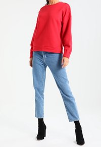 Rode sweatshirt met een ronde hals, lange mouwen en een relaxed fit, gecombineerd met lichtblauwe recht gesneden jeans en zwarte enkellaarsjes.