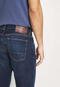 Dunkelblaue Denim-Jeans mit kontrastierendem gelbem Stitching. Verfügt über ein Lederlogo-Patch und sichtbare Gesäßtaschen.