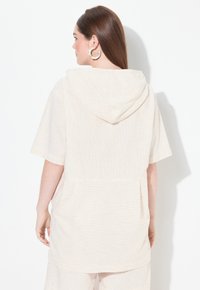 Top corto con capucha de manga corta en beige claro con finas rayas verticales, que presenta un corte holgado y una tela texturizada.