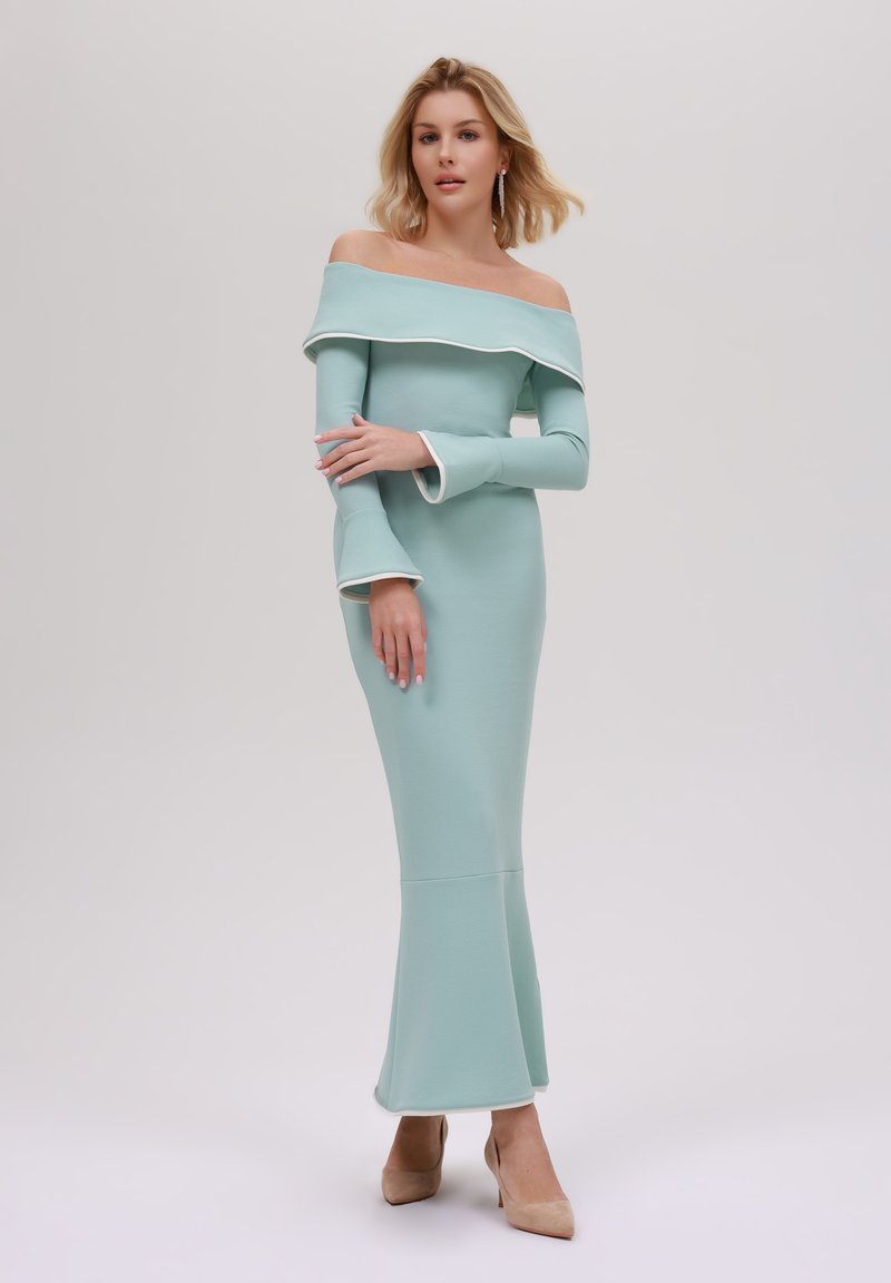 En figursydd, off-shoulder, mintgrön klänning med vit kant och lurviga ärmar, som sträcker sig till en utställd nederkant, kombinerad med nude klackar.