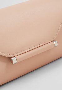 Pochette enveloppe en cuir rose doux avec une finition texturée, des détails en métal argenté et des coutures visibles le long des bords.