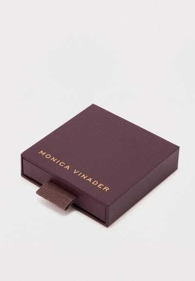 Caixa de presente bordeaux com textura suave e letras douradas "MONICA VINADER". Inclui uma aba de tecido para fácil abertura.