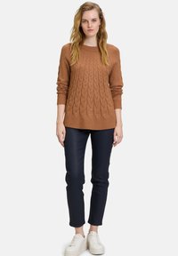 Brauner Strickpullover mit strukturiertem Design, kombiniert mit dunkelblauen Slim-Fit-Hosen und weißen Sneakern. Geeignet für die Freizeit.