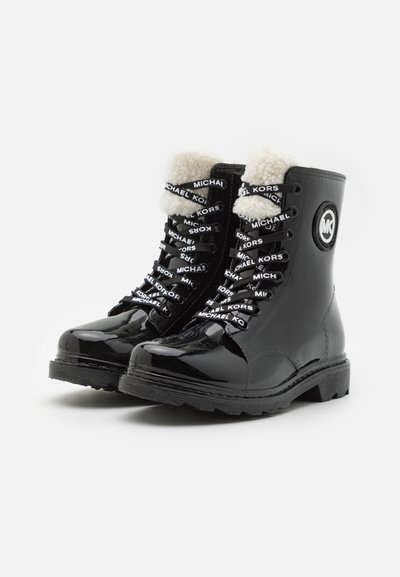 Bottines en cuir verni noir avec doublure en fausse fourrure blanche, dotées de lacets à logo et d'un logo rond sur le côté extérieur. Semelle texturée pour une meilleure adhérence.