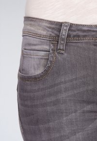 Šedé džínsy se slim fit střihem, pěti kapsami a kontrastním prošitím. Látka má mírně opotřebovaný vzhled s jemnými barevnými variacemi.