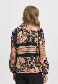 Blouse imprimée florale noire, avec des nuances de rose et d'or. Manches longues avec des poignets élastiques et coupe décontractée.