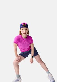 Sportoutfit bestehend aus einem leuchtend pinkfarbenen T-Shirt mit kurzen Ärmeln, marineblauen Shorts, weißen Turnschuhen und einer marineblauen Mütze mit pinker Unterseite.