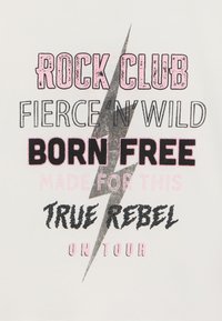 Hvit t-skjorte med forskjellig fet tekst i svart, rosa og sølv, med et lyn-design. Teksten inkluderer "Rock Club," "Born Free," og "True Rebel."