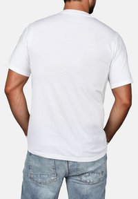 Weißes Baumwoll-T-Shirt mit kurzen Ärmeln, rundem Halsausschnitt und schlichter Rückseite, kombiniert mit hellblauen Jeans.