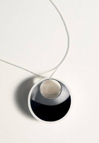 El collar con colgante circular presenta una superficie negra brillante con un acento plateado. Montado en una delgada cadena de plata, tiene un acabado liso y pulido.