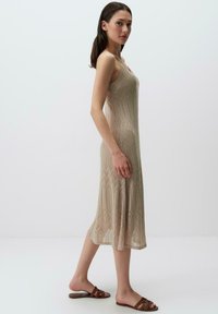  gebreide, mouwloze jurk in beige met een zigzagpatroon en een vloeiende silhouet, gecombineerd met bruin schuifsandalen.