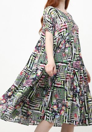 Leciutka sukienka do kolan z krótkimi rękawami, w geometryczne czarno-białe pasy oraz kolorowe kwiatowe wzory, noszona przez osobę o rudych włosach.