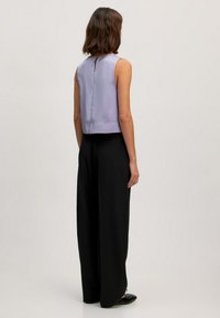 Geknipte, mouwloze blouse van lichtlila satijn, gecombineerd met loszittende zwarte broeken. Effen kleuren, gladde textuur, minimale details.