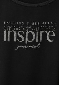 T-shirt nera con lettering in argento metallico testurizzato. Il testo include "Tempi Entusiasmanti In Arrivo", "ispira" e "la tua mente" in caratteri e stili diversi.