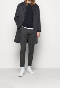 Grå ullrock, mörk tröja, grå byxor, vita strumpor och vita sneakers. Enkel design, rak passform och slät textur.