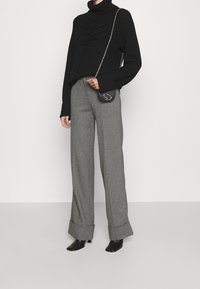 Jersey de cuello alto de canalé negro con un patrón texturizado, combinado con pantalones de pierna ancha grises. Los accesorios incluyen un pequeño bolso cruzado negro.