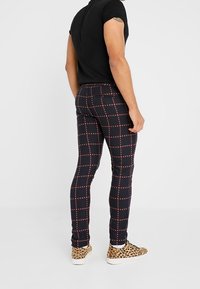 Zwart kortom shirt gecombineerd met marineblauwe geruite legging met een rood rasterpatroon, accentuerend met sneakers met luipaardpatroon.