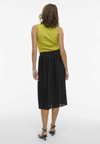 Haut sans manches vert lime associé à une jupe midi plissée noire fluide. La jupe présente une texture lisse et une taille ajustée.