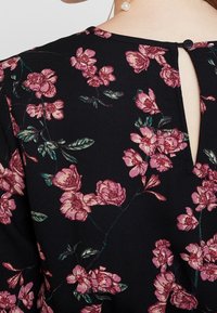 Black fabric top featuring a floral pattern in pink, with a keyhole back detail and small round button closure. Soft texture.