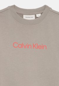 Grijze sweatshirt met een ronde halslijn en ribbels aan de mouwen, voorzien van het 'Calvin Klein' logo in fel koraal op de voorkant.