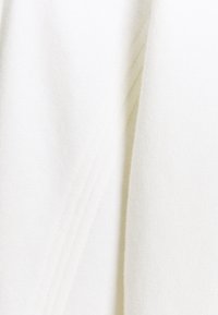 Gros plan sur un tissu tricoté doux et blanc montrant une texture fine et des plis subtils avec de légères ombres le long des coutures.