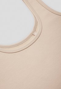 Beżowa koszulka na ramiączkach wykonana z gładkiego, elastycznego materiału, z okrągłym dekoltem oraz wzmocnionymi szwami wokół pach i u dołu.